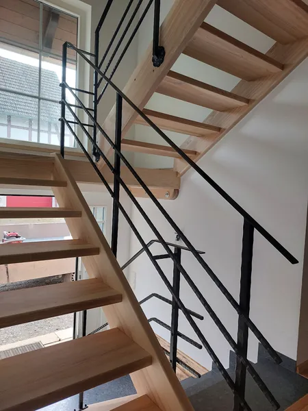 Durchgehendes Metallgeländer entlang einer offenen Holztreppe