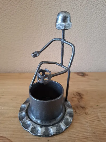 Kleine Metallfigur mit zylindrischem Gefäß auf einer Holzfläche